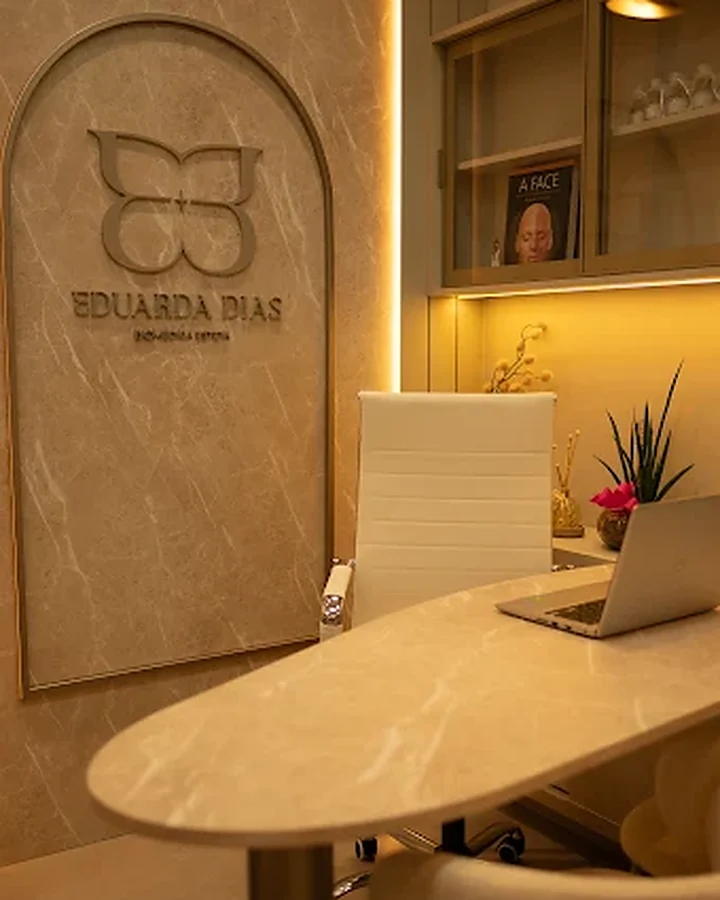 Sala de atendimento com mesa de mármore e a placa Eduarda Dias, Biomédica Esteta, na parede.
