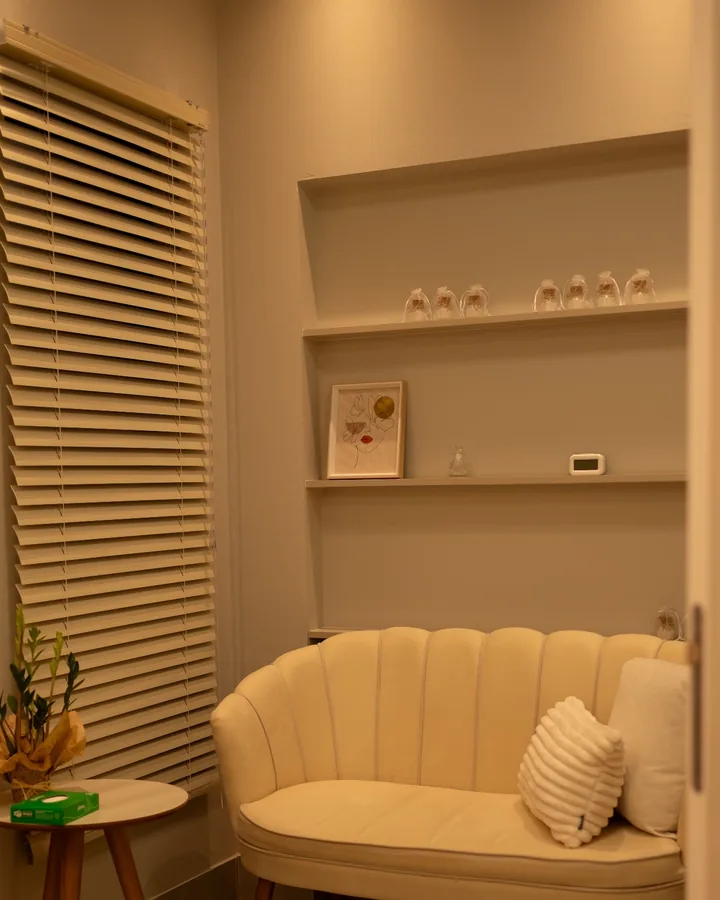 Sala de espera com sofá claro, mesa lateral e persiana de madeira.
